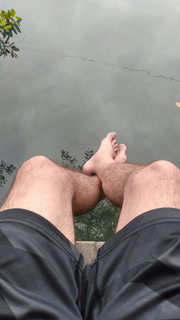 Bare feet dangling over the still green water of the Laguna de las Ninfas from the wooden dock, mangrove leaves at the edge of the frame